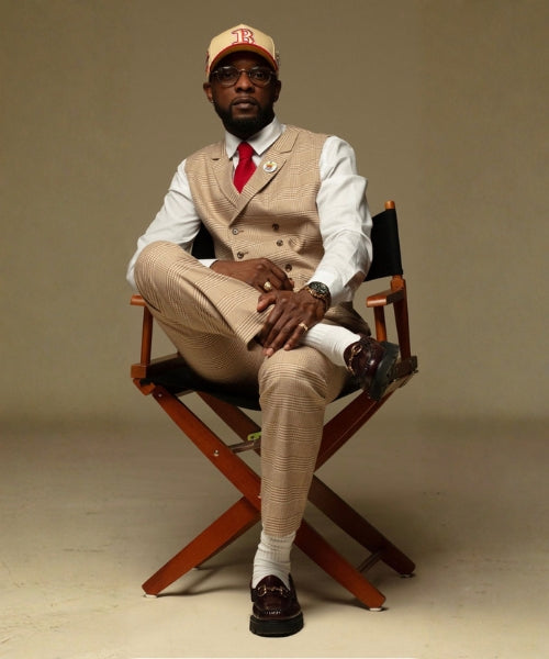 Man in formal attire sitting on a director's chair against a plain background