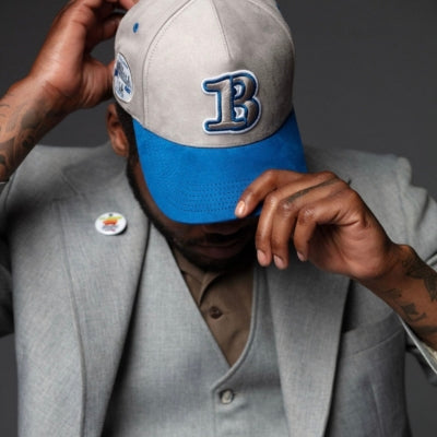Person wearing a gray and blue baseball cap with a 'B' logo, adjusting it with both hands.