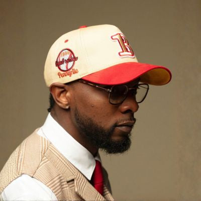 Man wearing a red and beige cap with a logo, glasses, and a beige vest over a white shirt.